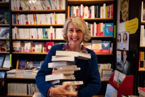 Portrait de Nathalie Iris dans sa librairie, les bras chargés de livres